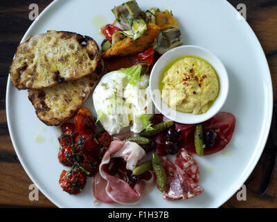 Un assortimento di prosciutti e verdure, serviti con salsa di pomodoro e il pane su una piastra bianca. Foto Stock