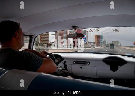 L'Avana, Cuba. Uomo cubano al lavoro di guida auto d'epoca, driver lavorando sul vecchio taxi, cabina nel traffico cittadino. Persone e trasporto Foto Stock