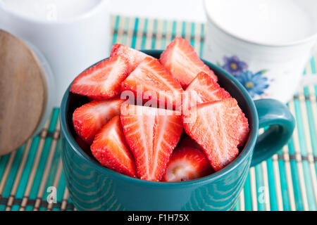 Dettaglio di fragole a fette in una ciotola con la tazza di latte e zucchero Foto Stock