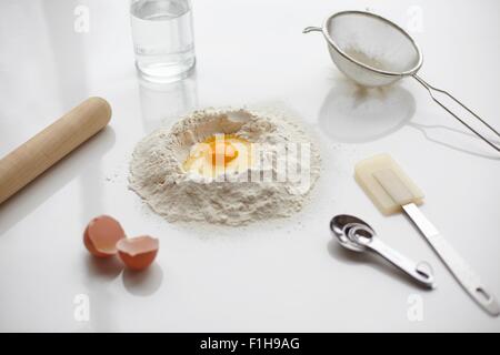 Preparazione di cottura con uovo crudo nel centro della pila di farina e utensili da cucina Foto Stock