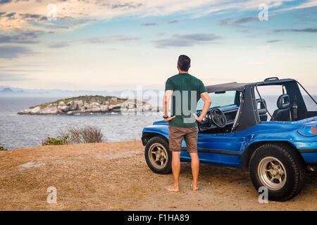 Vista posteriore del turista maschio guardando fuori per branca isola, Buzios, Rio de Janeiro, Brasile Foto Stock