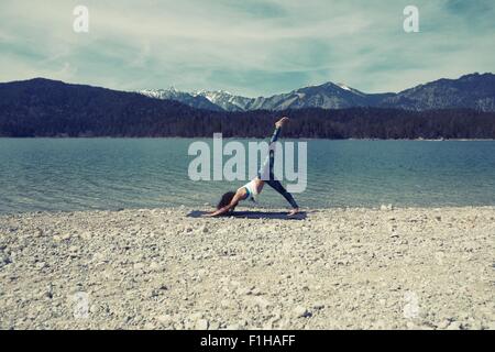 Metà donna adulta, accanto al lago, in posizione di yoga Foto Stock