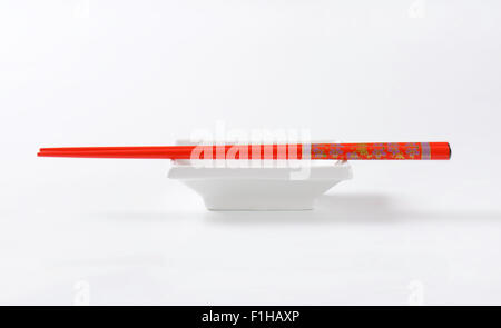 Coppia di bacchette rosso e ciotola bianco su sfondo bianco Foto Stock