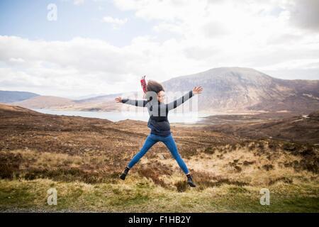 Metà donna adulta in montagna facendo star jump, Isola di Skye, Ebridi, Scozia Foto Stock