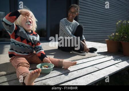 Ragazzo seduto su legno decking mangiare dalla ciotola Foto Stock