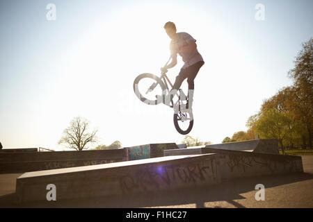 Giovane uomo, a metà in aria, facendo stunt su bmx a skatepark Foto Stock