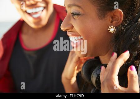 Close up profilo della giovane donna sorridente che indossano le cuffie, persone in background Foto Stock