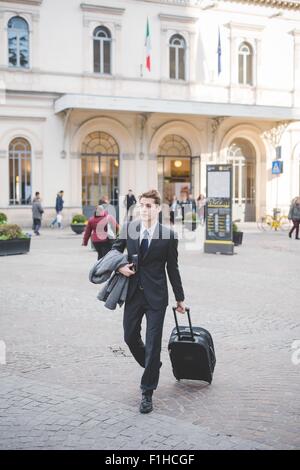 Giovane imprenditore commuter camminando lungo la strada di ciottoli con la valigia. Foto Stock