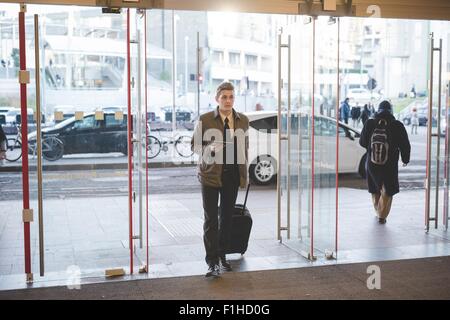 Giovane imprenditore commuter camminando attraverso delle porte in vetro con la valigia. Foto Stock