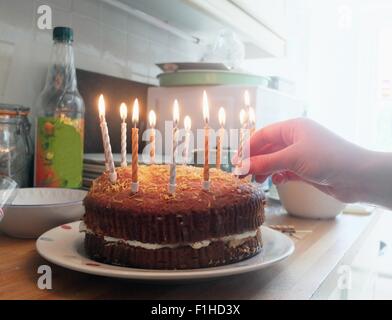 Mano di giovane donna mettendo candele accese sulla torta di compleanno Foto Stock