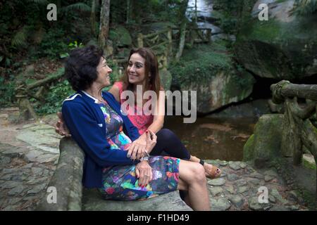 Donna Senior e figlia tenendo le mani sul fiume di bosco Foto Stock