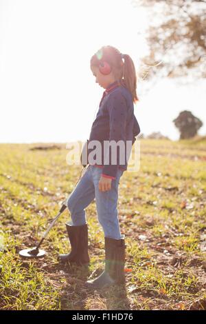 Ragazza che indossa le cuffie utilizzando il rilevatore di metallo nel campo Foto Stock