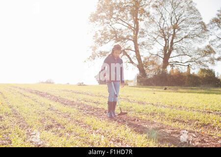 Ragazza che indossa le cuffie utilizzando il rilevatore di metallo nel campo soleggiato Foto Stock