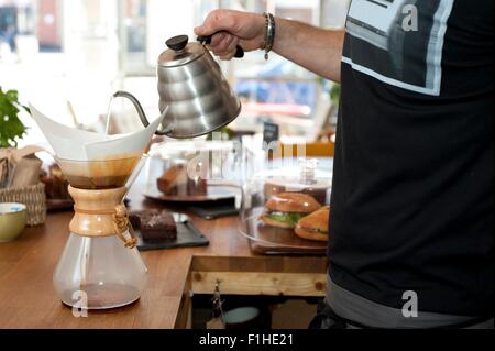 Mano del cafe cameriere versando acqua bollente nel filtro del POT del caffè Foto Stock