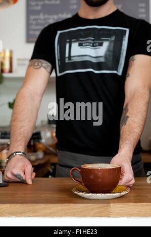 Ritagliato colpo di cameriere cafe che serve tazza di caffè fresco Foto Stock