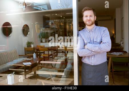 Ritratto di giovane maschio cafe proprietario con i bracci ripiegati in porta Foto Stock