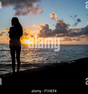 Silhouette di donna giovane la visione di sunrise, Kaaawa beach, Oahu, Hawaii, STATI UNITI D'AMERICA Foto Stock