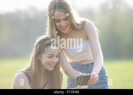 Due ragazze adolescenti che indossa daisy chain copricapo guardando fotografie istantanea in posizione di parcheggio Foto Stock