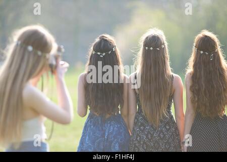 Vista posteriore della ragazza adolescente fotografare amici indossando daisy chain copricapo in posizione di parcheggio Foto Stock