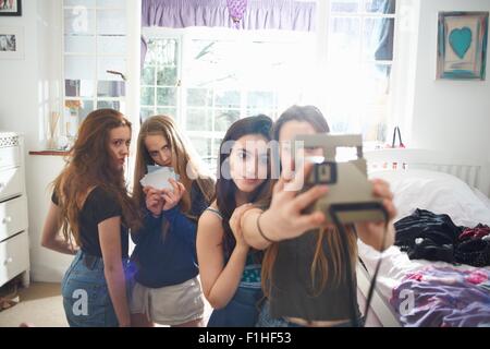Quattro ragazze adolescenti in camera da letto tenendo la fotocamera istantanea selfie Foto Stock