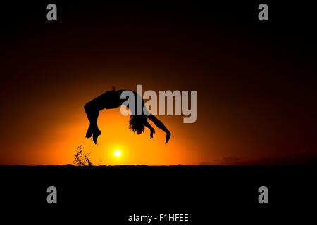 Silhouette di un uomo che fa del back flip, al tramonto, Omakaha, Oahu, Hawaii Foto Stock