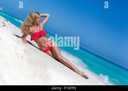 Slim concia di donna con capelli lunghi biondi che giace sulla spiaggia tropicale vicino al Mar dei Caraibi Foto Stock