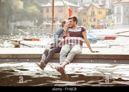 Giovane seduto sul molo whispering e mangiare il gelato in cono del lago di Mergozzo, Provincia di Verbania, Piemonte, Italia Foto Stock