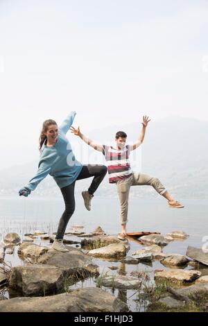 Giovane intensificazione su rocce con le braccia sollevate al Lago di Mergozzo, Provincia di Verbania, Piemonte, Italia Foto Stock