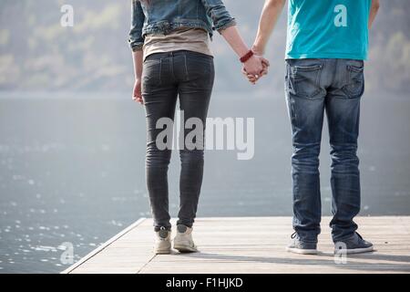 Tagliate vista posteriore della coppia giovane tenendo le mani sul molo presso il Lago di Mergozzo, Provincia di Verbania, Piemonte, Italia Foto Stock
