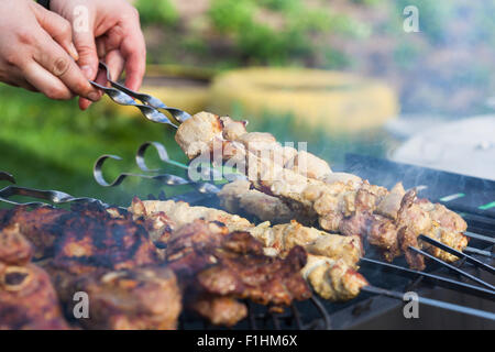 La cottura di bistecche di carne di agnello e maiale kebab sul grill, spiedini di carne di maiale in mano, all'aperto. Messa a fuoco selettiva e DOF poco profondo Foto Stock