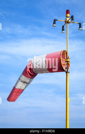 Indicatore del vento come un aeroporto attrezzatura. Rosso e bianco striato indicatore del vento su blu cielo nuvoloso Foto Stock