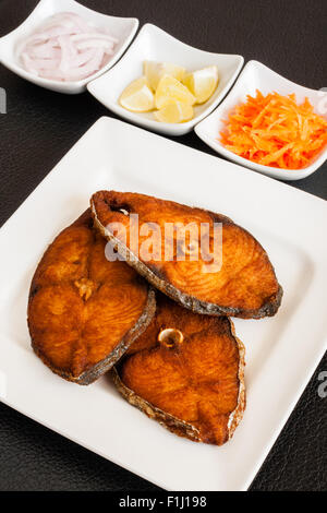 Primo piano della deliziosa seer/sgombro filetti di pesce fritto servito con le carote grattugiate, materie anelli di cipolla, limone. Foto Stock