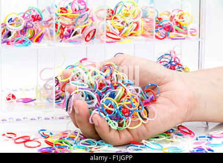 Mani e pila di rotondo piccolo gomma colorata bande di colore arcobaleno per rendere rainbow telaio braccialetti sul tavolo Foto Stock