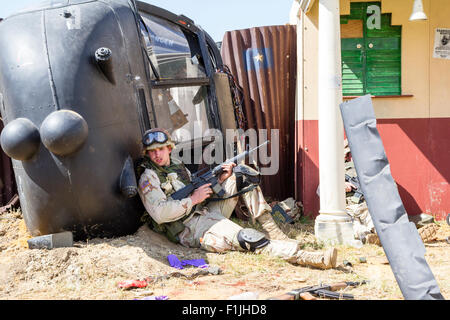 Esercito Americano, Black Hawk rievocazione. Stanco cercando soldato tenendo il coperchio mediante elicottero abbattuto, tenendo M16 rife pronto all'uso. Impostare a Mogadiscio. Foto Stock