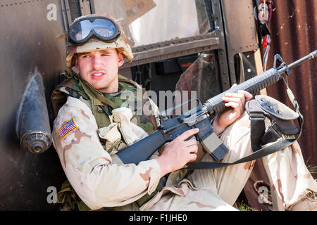 Esercito Americano, Black Hawk rievocazione. Stanco cercando soldato tenendo il coperchio mediante elicottero abbattuto, tenendo M16 rife pronto all'uso. Impostare a Mogadiscio. Foto Stock