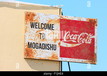 Guerra e pace rievocazione. La formazione di ruggine e stagionato vecchio segno sulla costruzione, "Benvenuti a Mogadiscio' e 'Coca-Cola', contro la luce blu sullo sfondo del cielo. Foto Stock