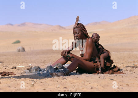 Himba donna e bambino seduto vicino a fuoco, Namibia, Africa Foto Stock