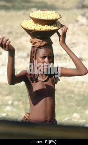 Himba ragazza in abito tradizionale che trasportano una ciotola sulla sua testa, Namibia Foto Stock