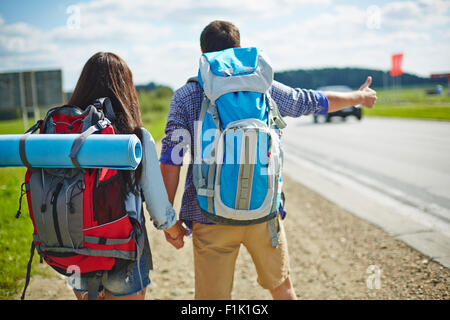 Coppia giovane di viaggiatori con zaino sollevatore-escursionismo su strada Foto Stock