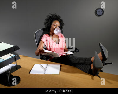 Annoiato donna soffiare bolle mentre è seduto alla sua scrivania Foto Stock