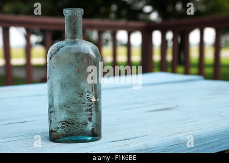 Antiquariato e oggetti in vetro soffiato medicina bottiglia visualizzata su un dipinto di blu, rustico tavolo da picnic. Foto Stock