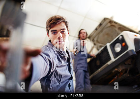 Mechanic raggiungendo per strumento sottostante auto nel negozio di riparazioni auto Foto Stock