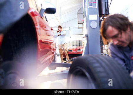 Il cliente parlando al telefono cellulare e controllare il tempo in negozio di riparazioni auto Foto Stock