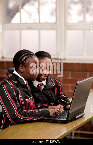 Due femmina di alta scuola gli studenti siedono insieme a una scrivania e lavorare su un laptop Foto Stock