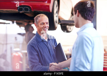 Meccanico e di handshaking del cliente in negozio di riparazioni auto Foto Stock