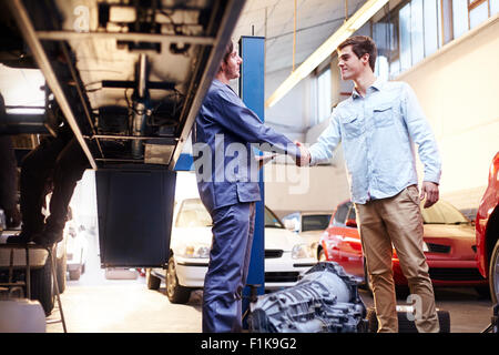 Meccanico e di handshaking del cliente in negozio di riparazioni auto Foto Stock