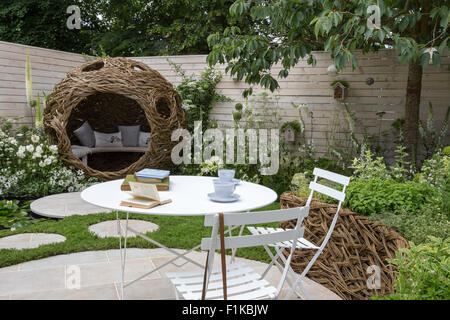 Piccolo spazio giardino urbano rotondo in pietra circolare patio tavolo sedie recinzione dipinta camomilla prato che scalda pietre fiori bianchi in Borders UK Foto Stock