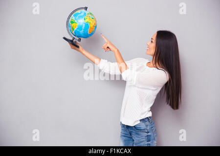 Ritratto di un felice bella donna di puntare il dito al mondo su sfondo grigio Foto Stock