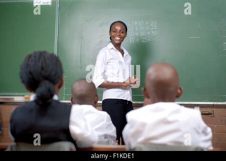 Insegnante africana scrivendo su una lavagna, insegnando la sua classe Foto Stock