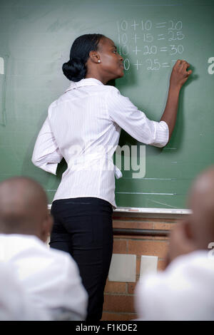 Insegnante africana scrivendo su una lavagna, insegnando la sua classe Foto Stock